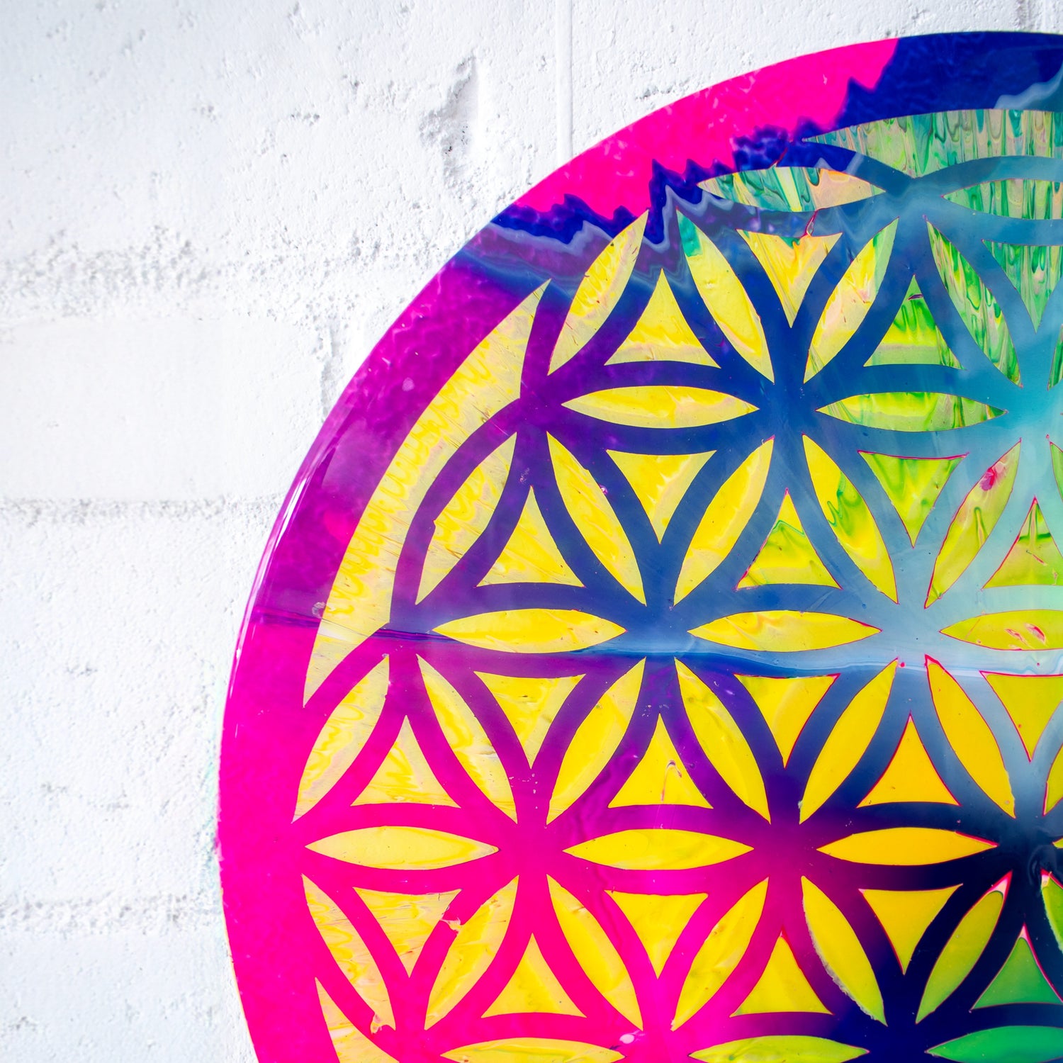 Callen Schaub’s cheerful circular painting, Càirdeas, features a blue and pink hand-stenciled flower-of-life lattice design over a diffuse yellow and green background using the artist’s signature pour and spin techniques. 